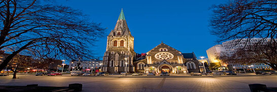 Nighttime view of Cathedral Square in Christchurch, New Zealand framed by silhouette of trees